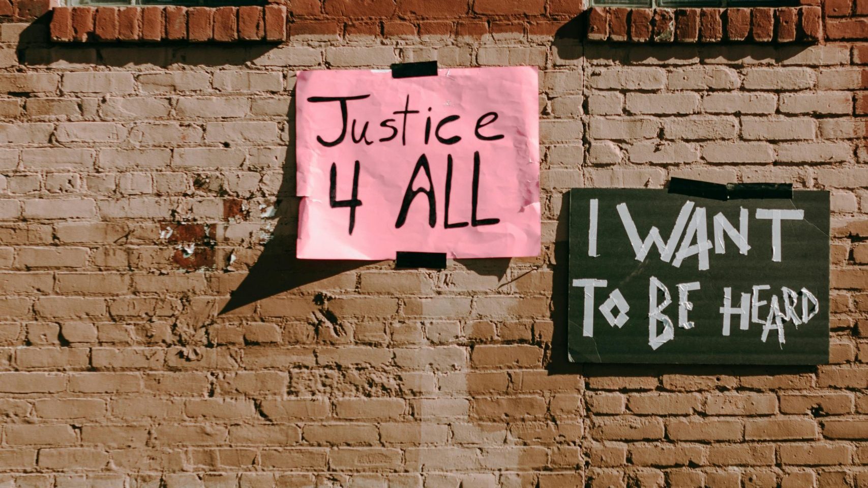 Street activism signs on a brick wall promoting social justice and freedom of speech.